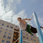 A young man skillfully balances on playground bars against a blue sky and urban backdrop.