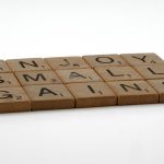 Close-up of Scrabble tiles forming the phrase 'Enjoy Small Gains' on a neutral background.